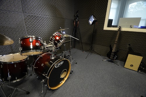 Sala de grabación musical, con batería, filmadora, luz.